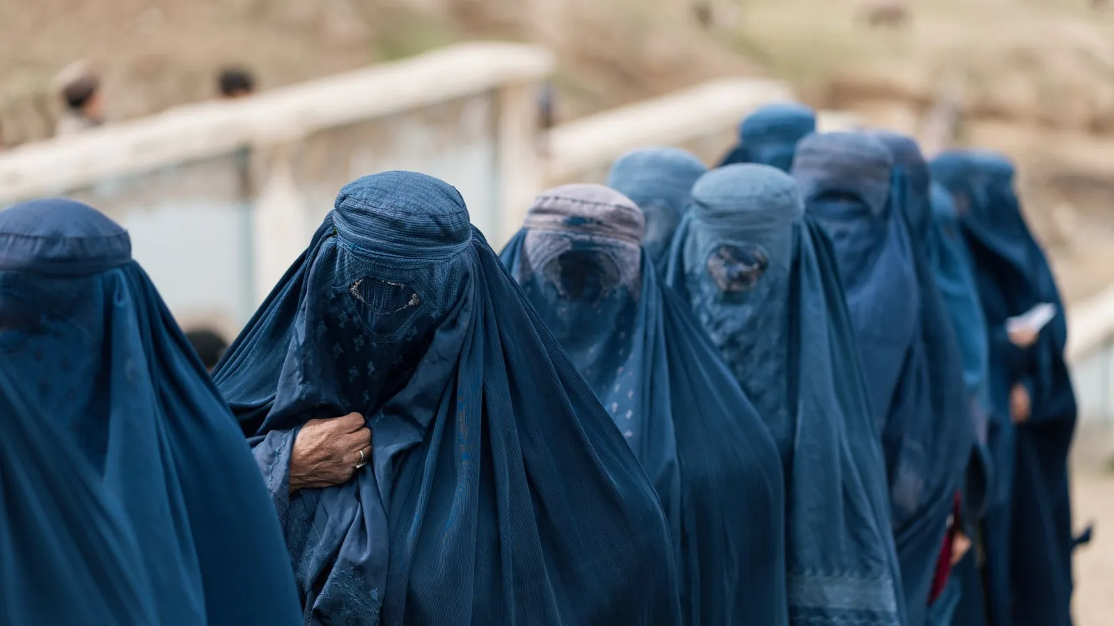 A group of women covered in blue burqas walking outdoors in Afghanistan, highlighting cultural attire.