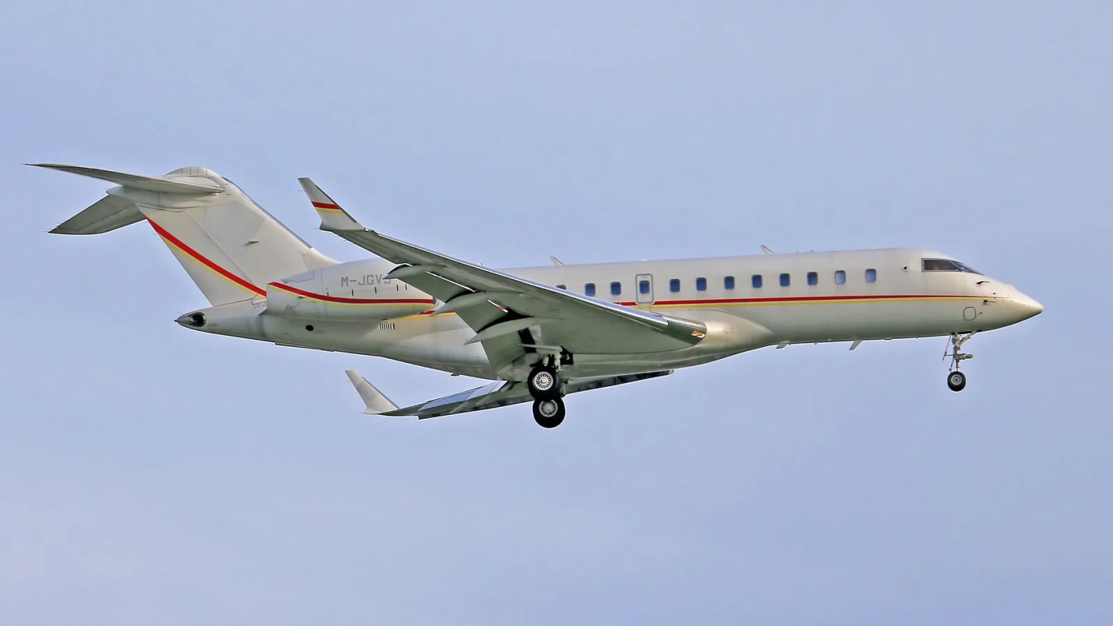 A sleek Bombardier Global Express jet in flight against a clear blue sky.