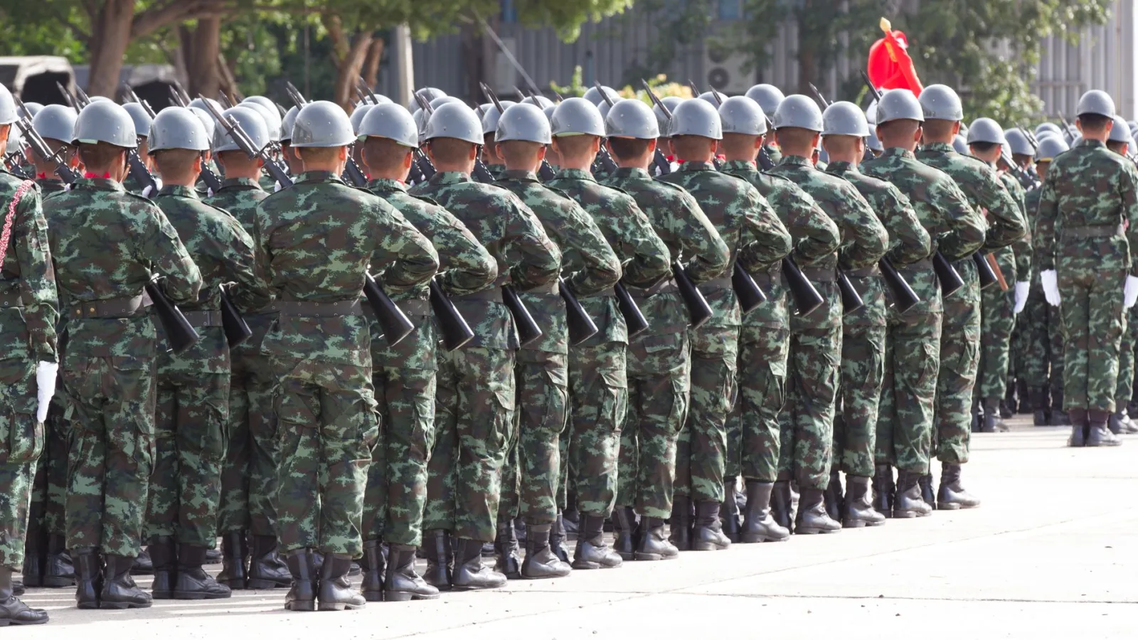Back view unrecognizable soldiers with riffles wearing khaki uniform and hardhat lining up in rows during military ceremony