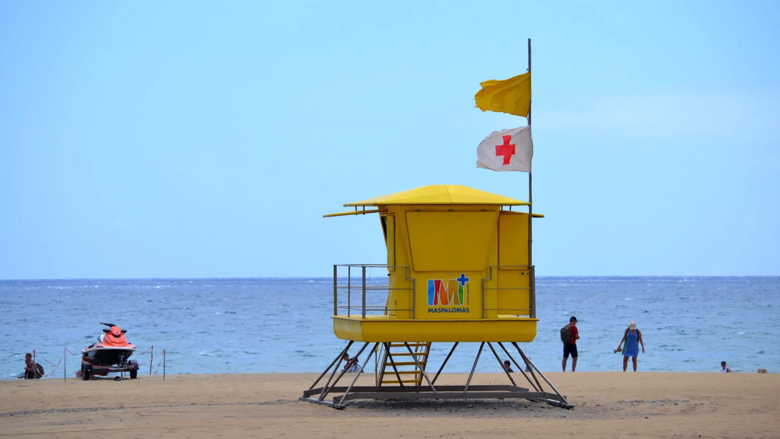 Lifeguard tower with flags on Maspalomas beach, Spain, with people enjoying summer.