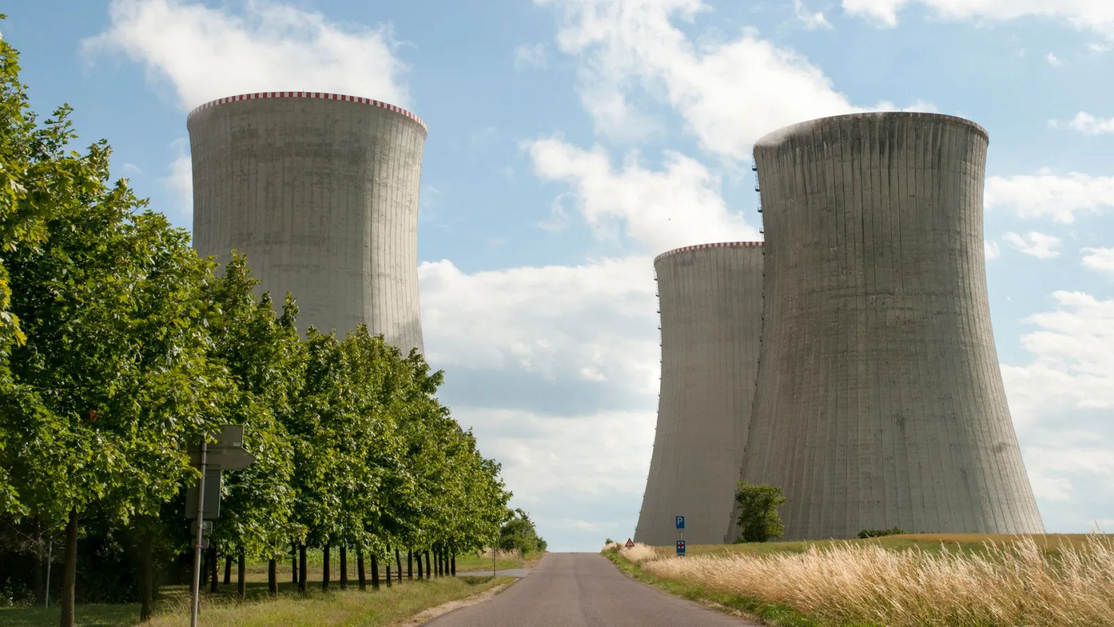 A nuclear power plant cooling towers by a road with green trees under a clear sky.