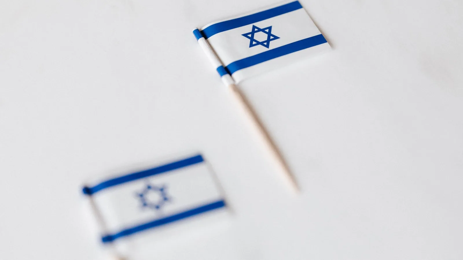 From above of small flags of Israel on toothpicks placed on white surface