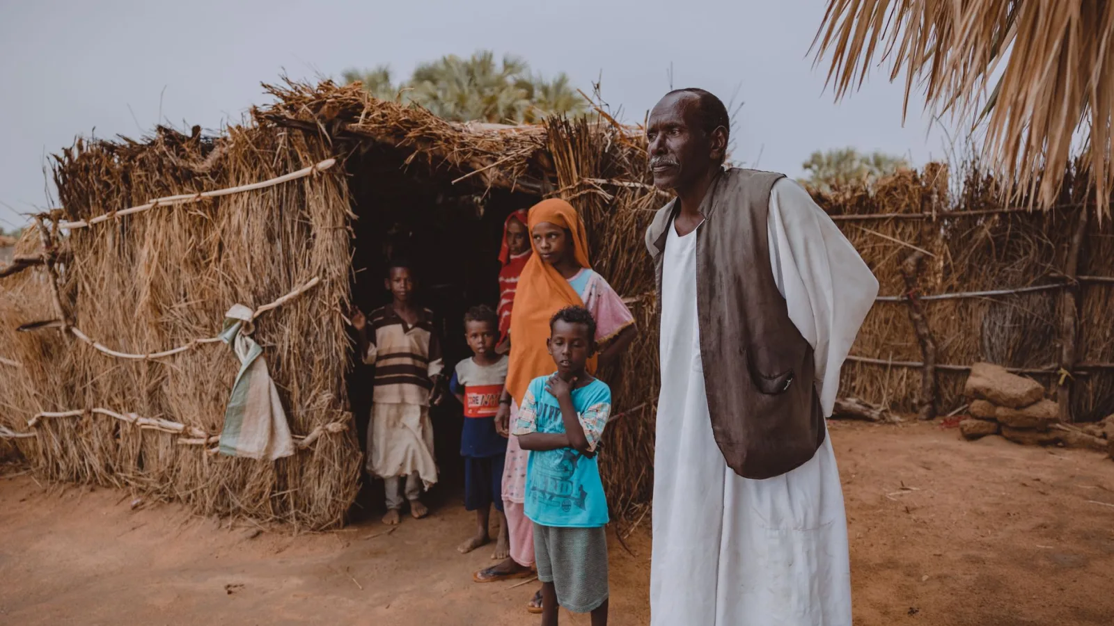Portrait of family standing outside a traditional straw hut in a rural village.