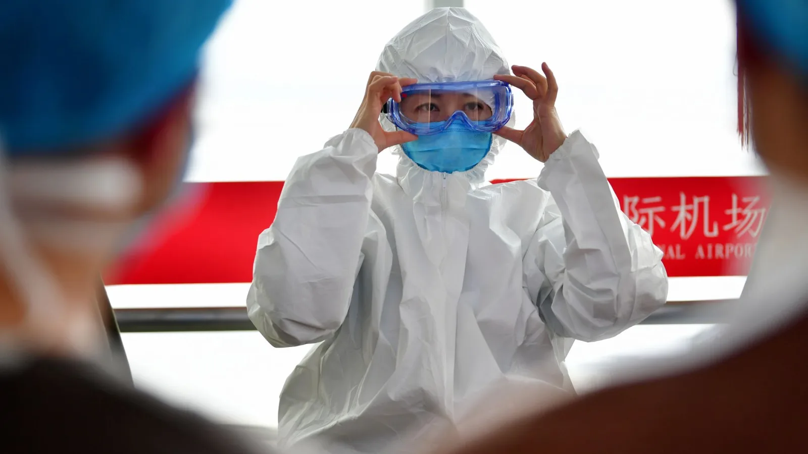 A healthcare professional dons protective clothing at an airport, highlighting safety measures during a pandemic.