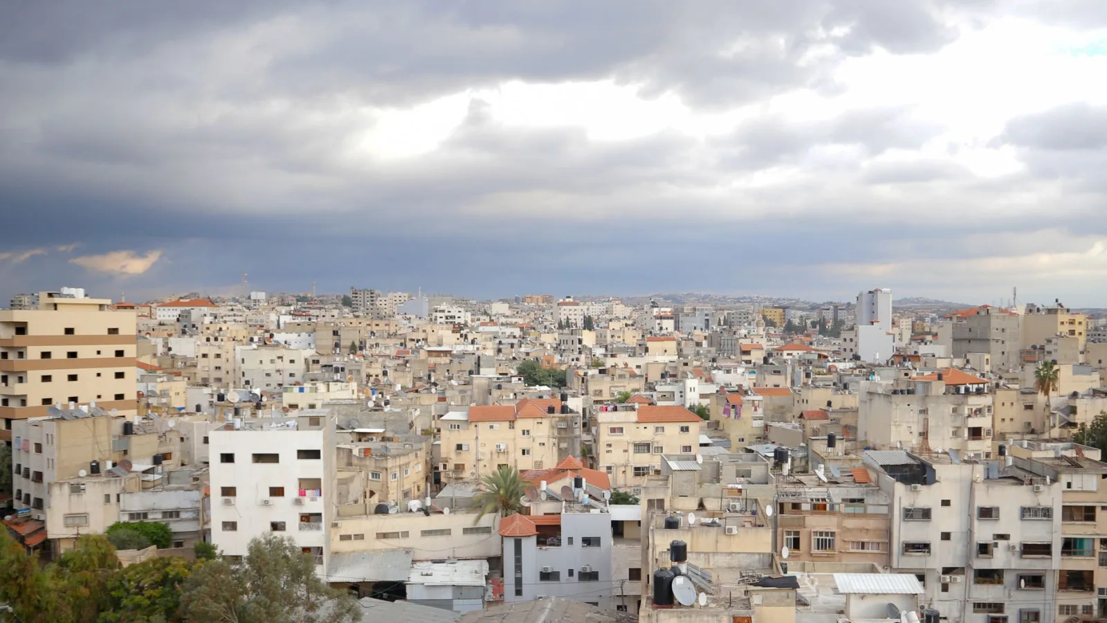 Aerial view of Qalqilya's urban cityscape under dramatic clouds, showcasing diverse architecture.