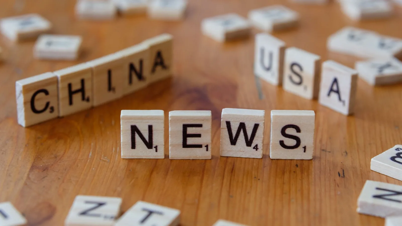 Wooden Scrabble tiles spelling 'NEWS' with 'CHINA' and 'USA' on a wooden surface.