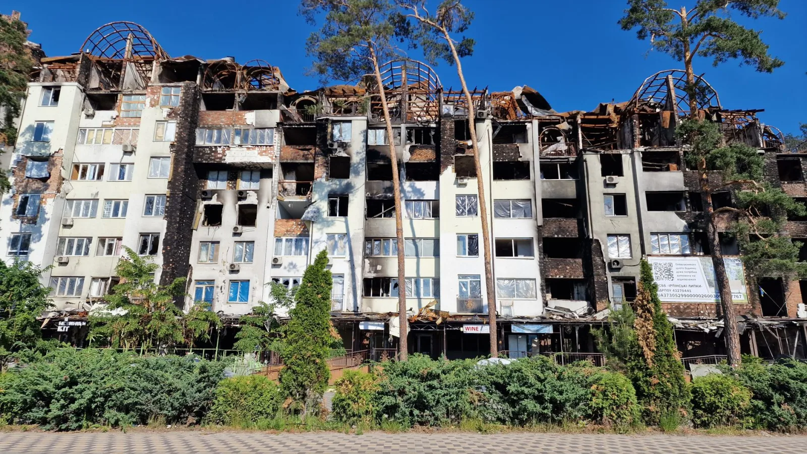 Exterior view of a ruined apartment building in Irpin, Ukraine under a clear blue sky.