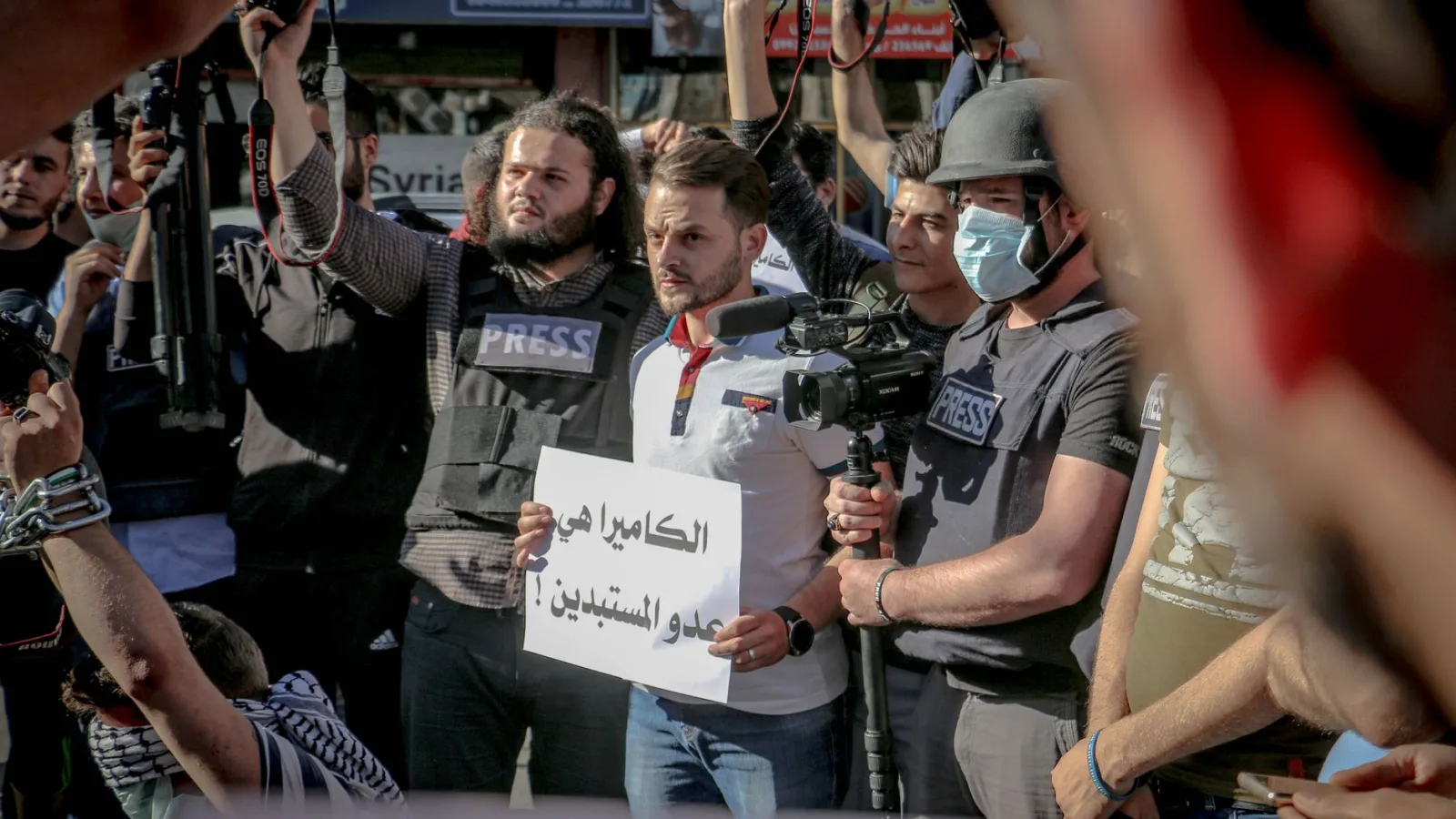 Group of ethnic journalists with placard with Arabic inscription and cameras at demonstration against policy