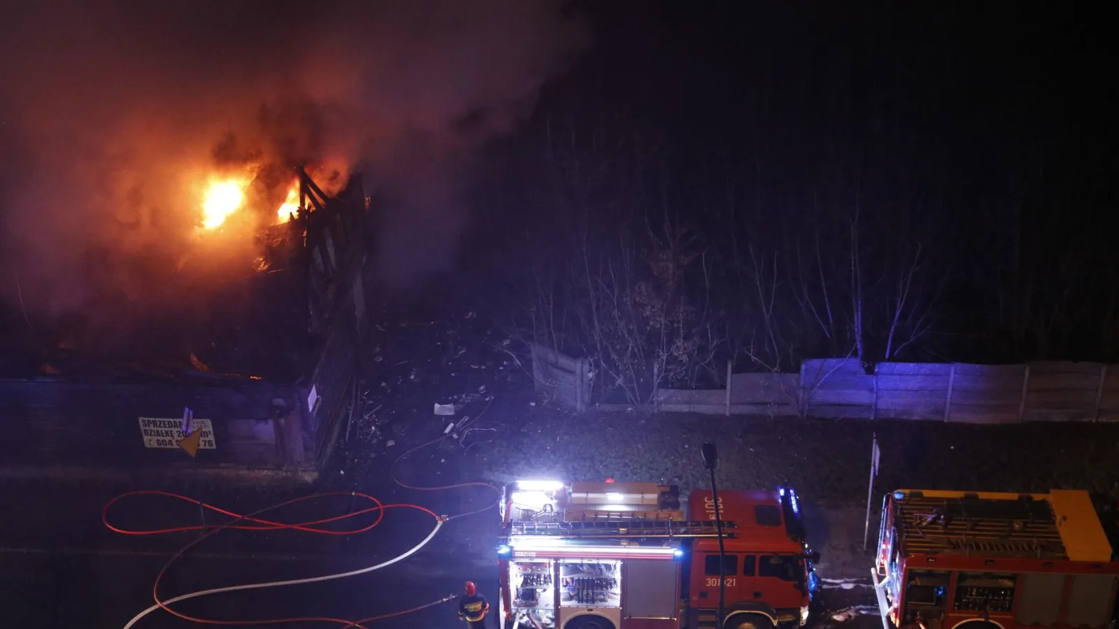 Aerial view of firemen tackling a nighttime building blaze with fire trucks on scene.