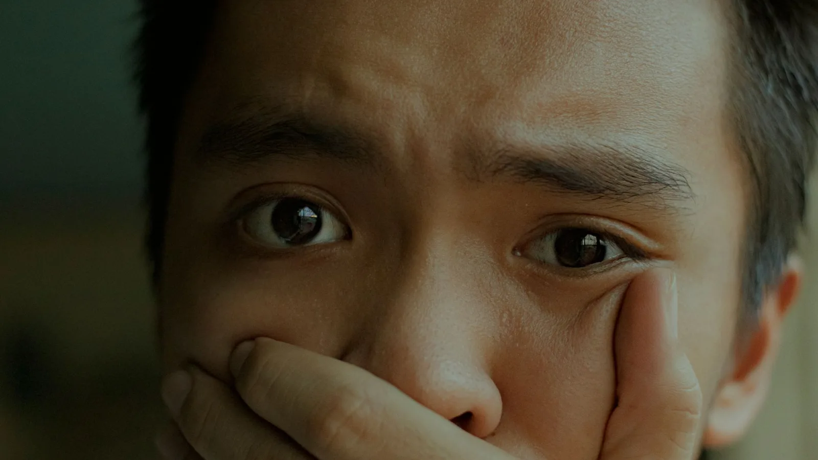 A young man with a distressed expression, covering his mouth.