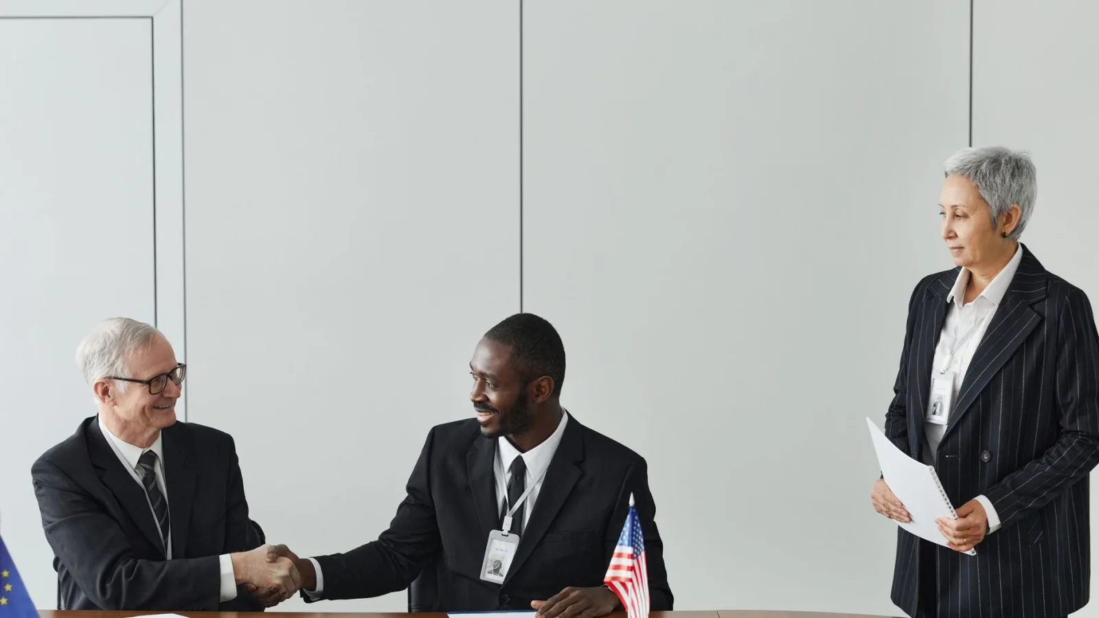 Multinational business meeting with agreement signing, featuring diverse professionals and flags.