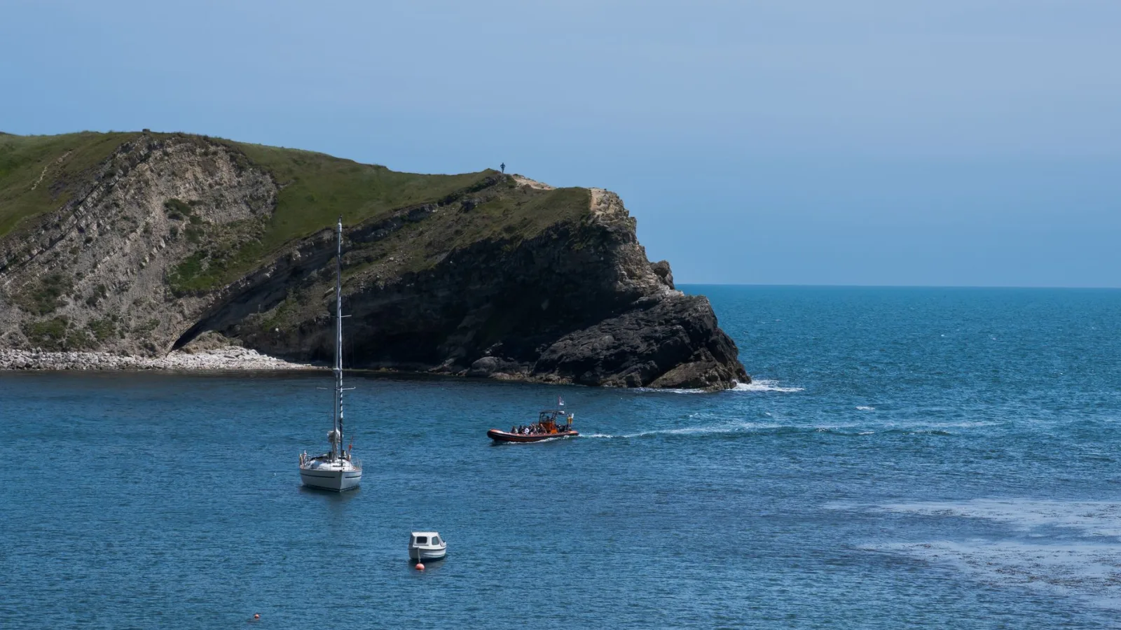 Beautiful coastal scene of Lulworth Cove in England with sailboats and cliffs in view.