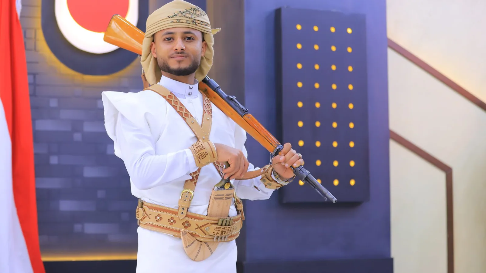 A man in traditional Yemeni dress poses with a rifle indoors in Sana'a, Yemen.