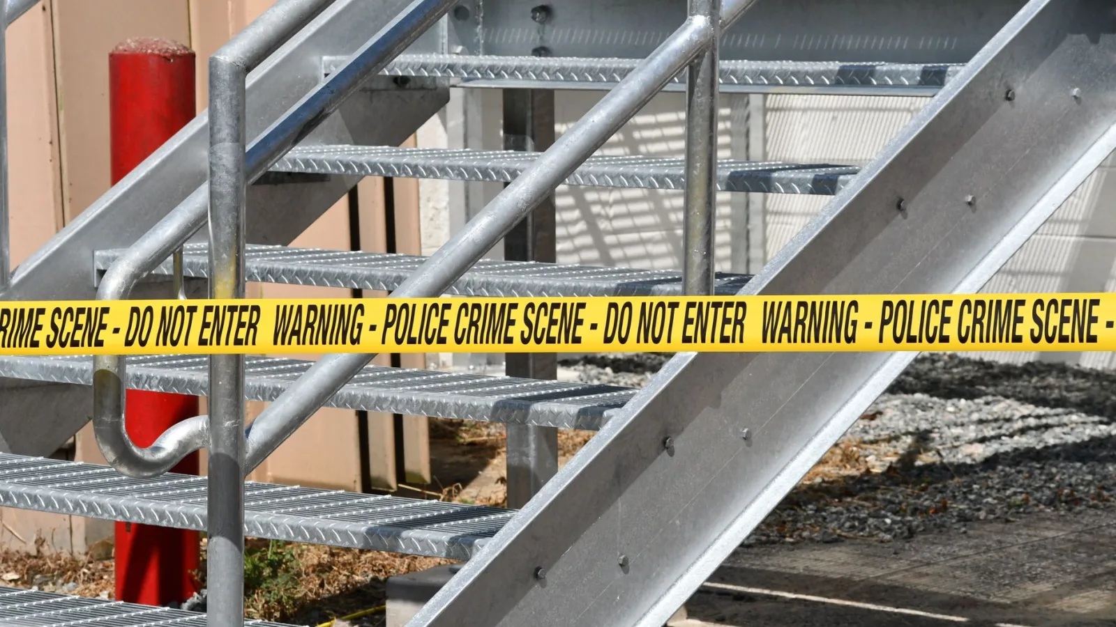 Close-up of a metal stairway blocked by yellow police crime scene tape outdoors.