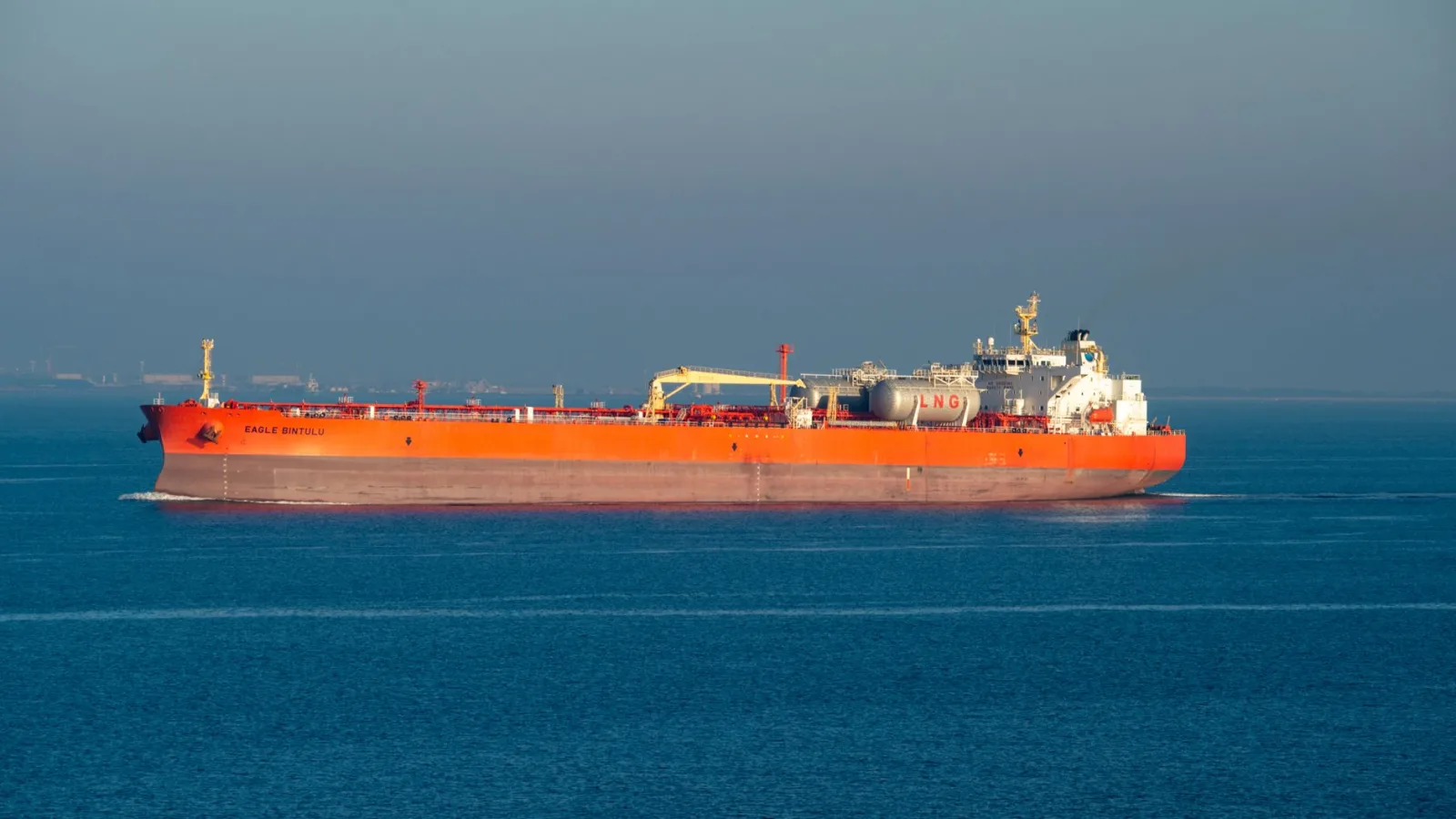 Bright orange LNG carrier ship cruising through calm sea waters on a clear day.