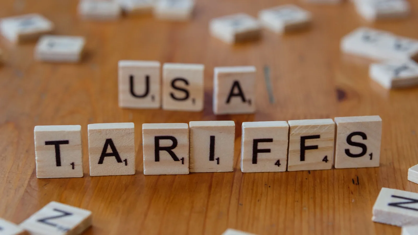 Wooden tiles spelling 'USA' and 'TARIFFS' on a wooden surface symbolizing trade issues.