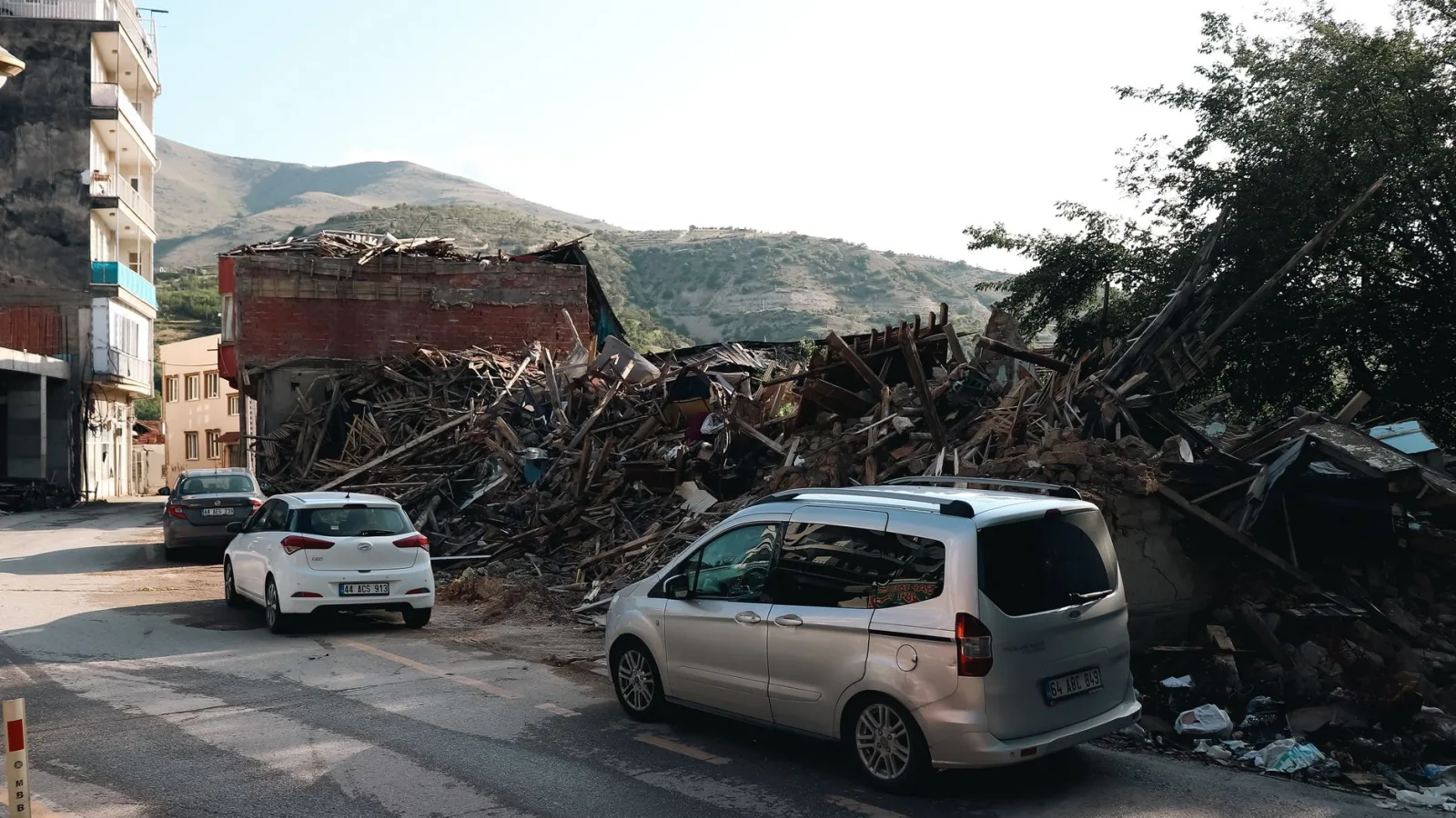 A city street with cars passing by buildings destroyed by an earthquake.