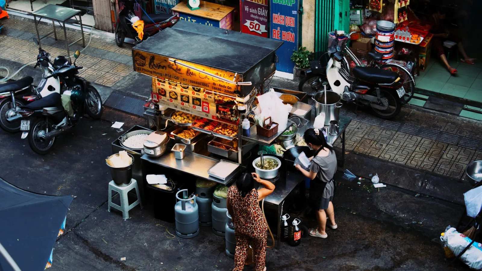 Two women preparing food at a bustling Vietnamese street food stall.