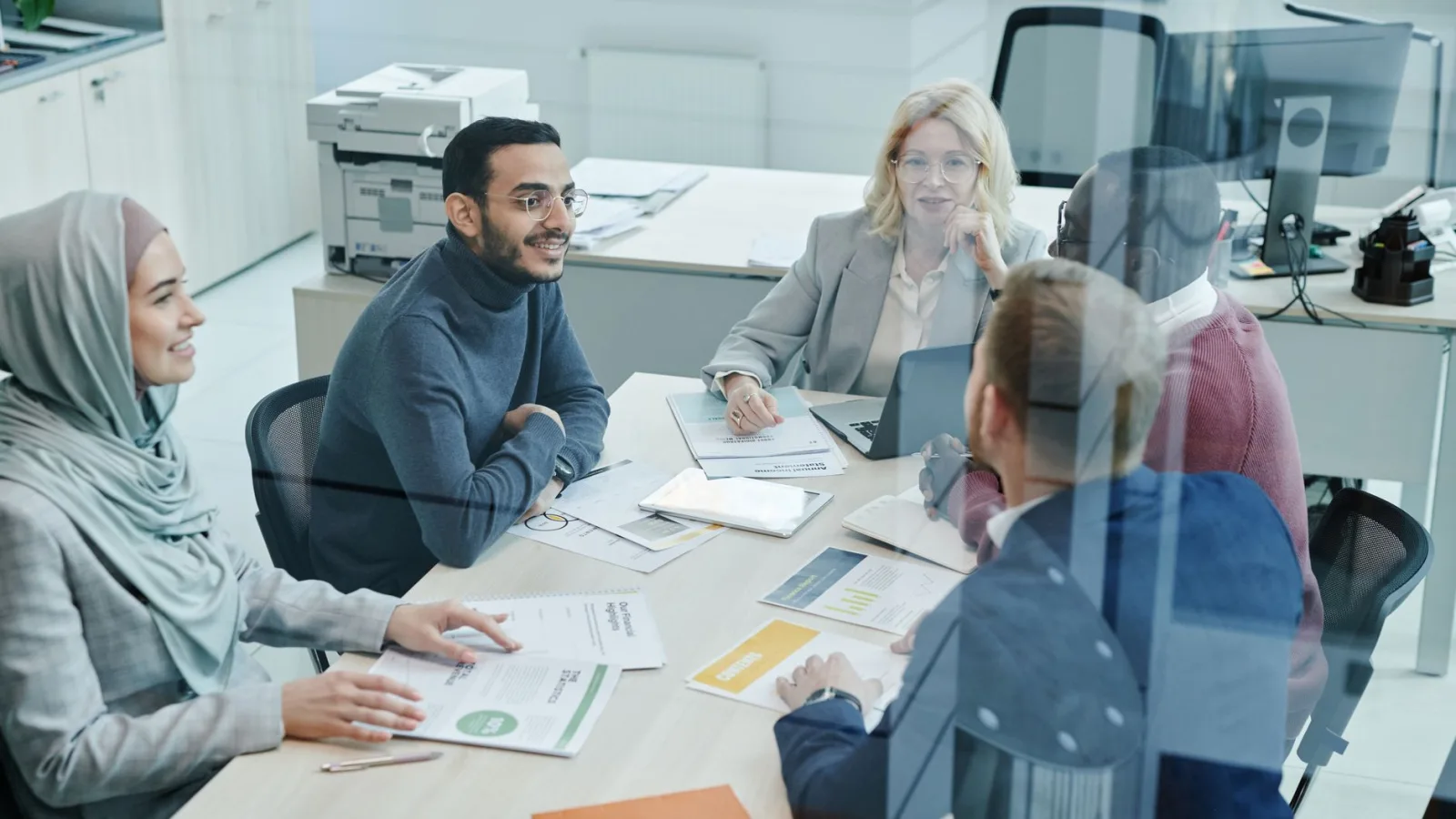 A diverse group of professionals engaged in a meeting at a modern office, promoting teamwork and collaboration.